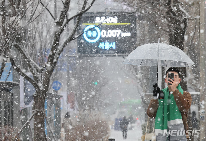 [서울=뉴시스] 김근수 기자 = 수도권 등에 대설주의보가 내려진 30일 오후 3시 기준 서울엔 12㎝가 넘는 눈이 쌓였다. 서울지역에 대설주의보가 내려진 30일 서울 종로구 세종대로 일대에서 한 시민이 휴대전화에 내리는 눈을 담고 있다. 2023.12.30. ks@newsis.com