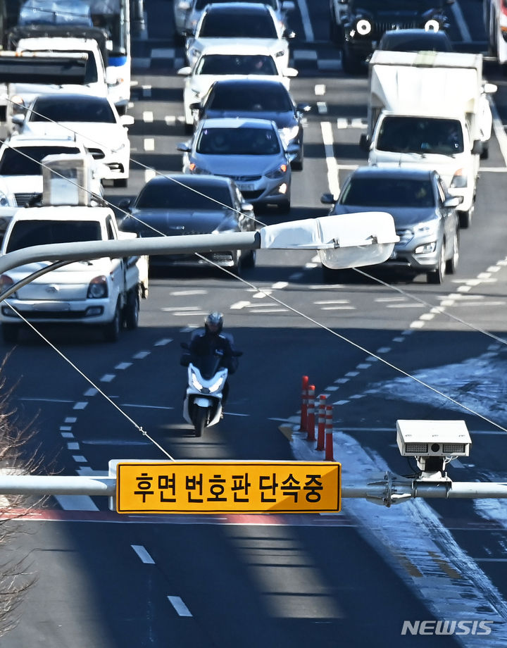 [수원=뉴시스] 김종택 기자 = 8일 경기도 수원시 한 도로에 설치된 후면 무인교통 단속 카메라 앞을 오토바이 운전자가 지나가고 있다. 경찰청은 오늘부터 뒷번호판을 찍는 후면 단속카메라를 활용해 이륜차 신호·과속 단속과 안전모 미착용을 무인 단속한다고 밝혔다. 2024.01.08. jtk@newsis.com