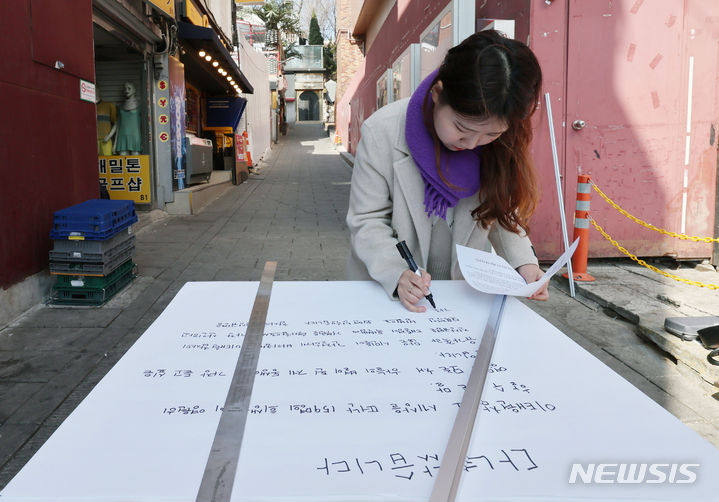 [서울=뉴시스] 김진아 기자 = 21일 서울 이태원역 1번 출구 앞 이태원참사 추모의 벽에서 10.29 이태원참사 희생자 유연주의 언니 유정이 2030 세대에게 호소하는 대자보를 작성하고 있다.  2024.03.21. bluesoda@newsis.com