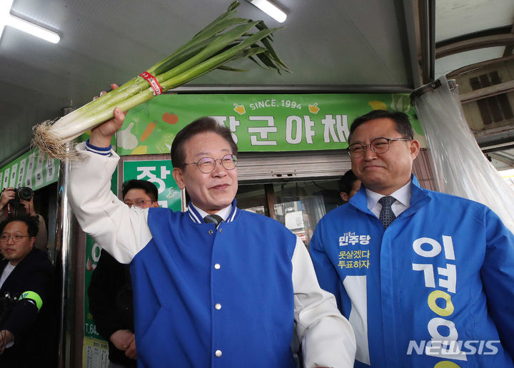 [제천=뉴시스] 이영환 기자 = 이재명 더불어민주당 대표가  27일 오후 충북 제천시 동문전통시장에서 시민들에게 인사를 하며 대파를 들어보고 있다. 오른쪽은 이경용 제천·단양 후보. (공동취재) 2024.03.27. photo@newsis.com