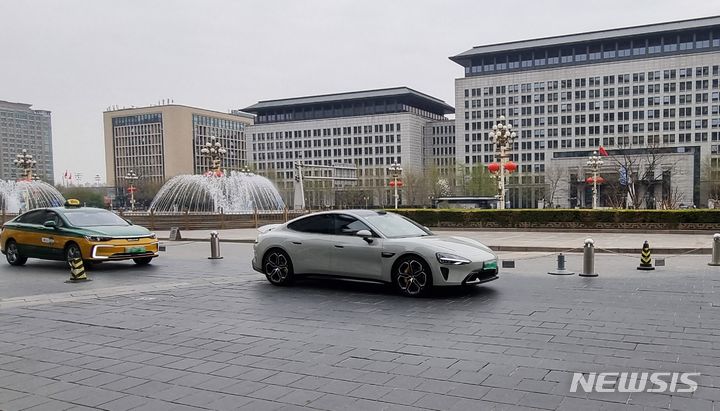 [베이징=뉴시스]박정규 특파원 = 1일 중국 베이징 둥펑구 왕푸징 거리의 한 쇼핑몰 앞에서 샤오미의 첫 전기차 SU7 차량이 지나가고 있다. 2024.4.1 pjk76@newsis.com