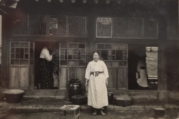 [서울=뉴시스]1950년대 최종건 SK 창업회장과 최종현 선대회장의 모친인 이동대 여사가 한옥 부엌 앞에서 식사를 준비하고 있다. (사진 = SK) 2024.04.08. photo@newsis.com&nbsp; *재판매 및 DB 금지