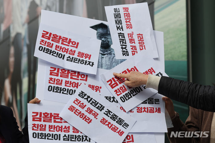 [서울=뉴시스] 권창회 기자 = 이화여대 동문들이 8일 오후 서울 서대문구 이화여대 정문 앞에서 열린 김활란의 친일-반여성 행각을 직시하며 역사 앞에 당당한 이화인을 바라는 기자회견에서 김활란 이화여자대학교 초대 총장 동상 그림에 손피켓을 붙이는 퍼포먼스를 하고 있다. 2024.04.08. kch0523@newsis.com