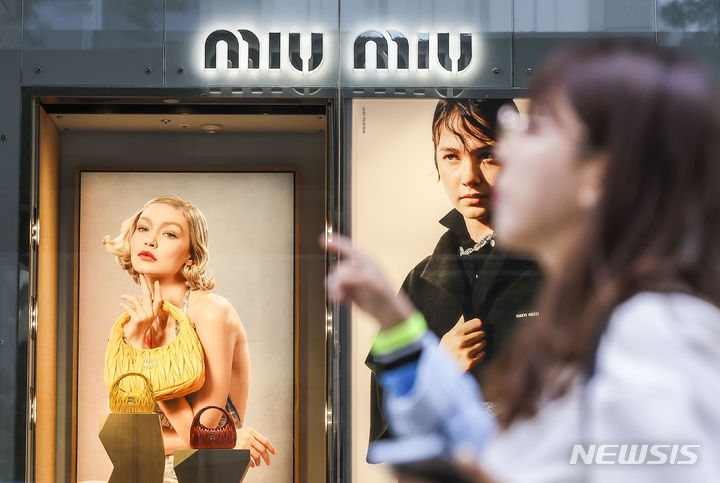 [서울=뉴시스] 정병혁 기자 = 7일 서울시내 백화점 미우미우 광고판 앞에서 시민들이 이동하고 있다. 프라다 계열의 명품 브랜드 '미우미우'가 최근 일부 제품에 대해 가격 인상을 단행했다. 미우미우는 이달 초 별도 공지 없이 일부 제품의 가격을 올린 것으로 확인됐다. 인기 제품인 아르카디 시리즈는 7~9% 가량 올랐다. 대표적으로 '아르카디 마테라쎄 나파 가죽 백'은 365만원에서 400만원으로 약 9.6%, '아르카디 가죽 백 미디움'은 390만원에서 420만원으로 약 7.7% 인상했다. 2024.05.07. jhope@newsis.com
