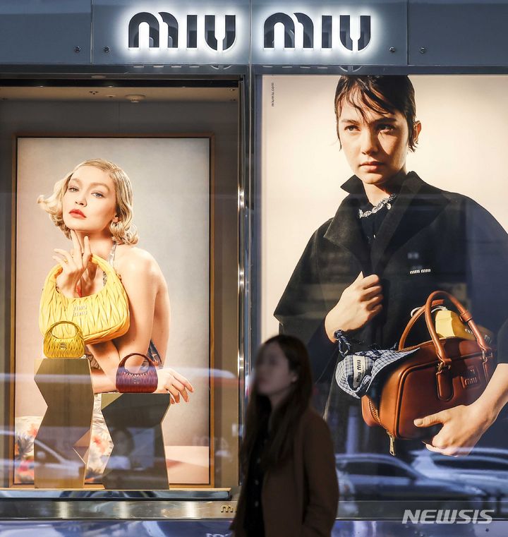 [서울=뉴시스] 정병혁 기자 = 7일 서울시내 백화점 미우미우 광고판 앞에서 시민들이 이동하고 있다. 프라다 계열의 명품 브랜드 '미우미우'가 최근 일부 제품에 대해 가격 인상을 단행했다. 미우미우는 이달 초 별도 공지 없이 일부 제품의 가격을 올린 것으로 확인됐다. 인기 제품인 아르카디 시리즈는 7~9% 가량 올랐다. 대표적으로 '아르카디 마테라쎄 나파 가죽 백'은 365만원에서 400만원으로 약 9.6%, '아르카디 가죽 백 미디움'은 390만원에서 420만원으로 약 7.7% 인상했다. 2024.05.07. jhope@newsis.com