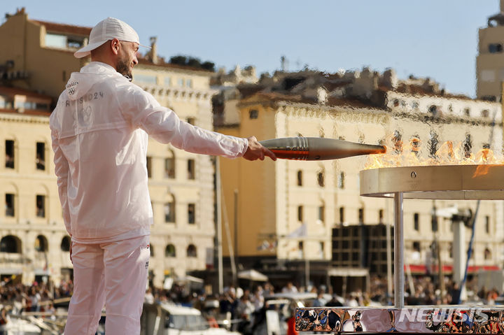 [마르세유=AP/뉴시스] 8일(현지시각) 프랑스 마르세유에서 열린 2024 파리올림픽 성화 환영식에서 프랑스 래퍼 줄이 성화를 성화대에 옮기고 있다. 2024.05.09.
