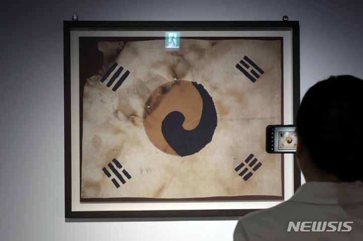 [서울=뉴시스] 최동준 기자 = 13일 서울 덕수궁 돈덕전에서 열린 문화유산국민신탁 소장유물특별전 '국봉' 전시를 찾은 시민이 진관사 소장 태극기 영인본을 관람하고 있다. 2024.05.13. photocdj@newsis.com