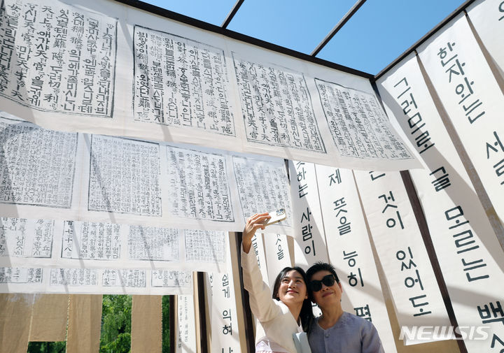 [서울=뉴시스] 김금보 기자 = 14일 오후 서울 종로구 경복궁에서 627돌 세종대왕 나신 날을 기념해 열린 '세종과의 하루, 세종대왕 탄신 하례연' 행사를 찾은 관람객들이 훈민정음을 활용한 전시물을 배경으로 추억을 담고 있다. 2024.05.14. kgb@newsis.com