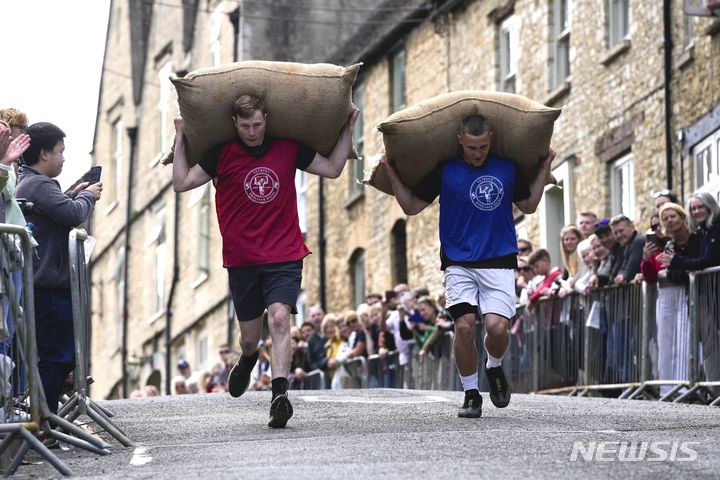 [테트베리=AP/뉴시스] 27일(현지시각) 영국 글로스터셔주 테트베리에서 연례 '울색 레이스'(Woolsack Race)가 열려 참가자들이 울색(양털 포대)을 짊어지고 언덕을 오르고 있다. 1972년 시작된 이 대회는 코로나19로 중단됐다가 재개됐다. 성인 남자는 27㎏, 여자는 16㎏의 포대를 메고 약 256m 코스의 언덕을 달리며 어린이 부문도 있다. 2024.05.28.