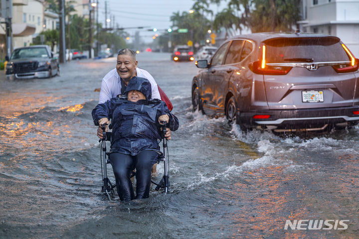 [마이애미비치=AP/뉴시스] 12일(현지시각) 미 플로리다주 마이애미비치에서 한 남성이 휠체어에 앉은 부인을 밀며 폭우로 침수된 거리를 건너고 있다. 플로리다주 마이애미와 포트로더데일 등에 시간당 최대 200㎜가 넘는 폭우가 내려 남부 전역에 홍수가 발생, 거리가 물에 잠기고 항공편이 취소됐다. 2024.06.13.