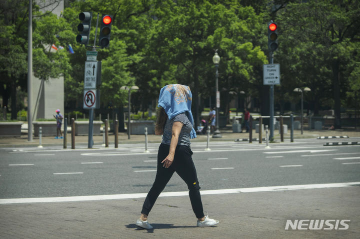 [워싱턴=AP/뉴시스] 19일(현지시각) 미국 워싱턴에서 한 여성이 햇볕을 피하기 위해 옷을 머리에 쓴 채 걷고 있다. 2024.06.20.