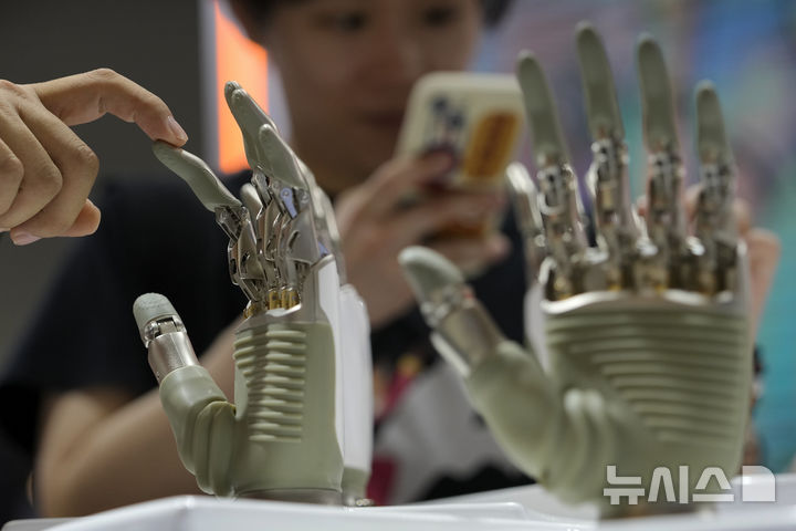 [상하이=AP/뉴시스] 상하이 엑스포 센터 다목적 홀 AI 전시 부스에서 한 방문객이 전시된 휴머노이드 로봇의 손을 만지고 있다. 2024.07.04.