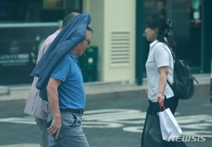 [서울=뉴시스] 고범준 기자 = 전국적으로 장맛비가 내리는 16일 오후 서울 중구 명동거리 인근에서 한 시민이 겉옷으로 비를 피하며 지나가고 있다. 2024.07.16. bjko@newsis.com