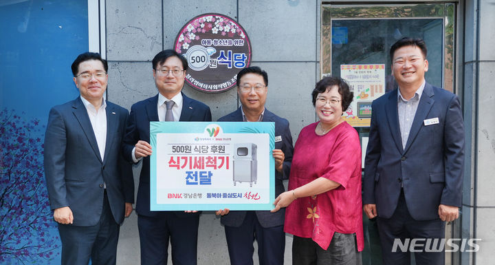 [창원=뉴시스]경남 창원특례시 진해구 '500원 식당' 앞에서 BNK경남은행 최대식(왼쪽서 두 번째부터) 사회공헌홍보부장이 창원특례시 정현섭 구청장, '500원 식당' 운영기관인 블라썸여좌사회적협동조합 이영순 이사장에게 식기세척기 기탁증서를 전달하고 있다.(사진=BNK경남은행 제공)2024.07.19.photo@newsis.com 