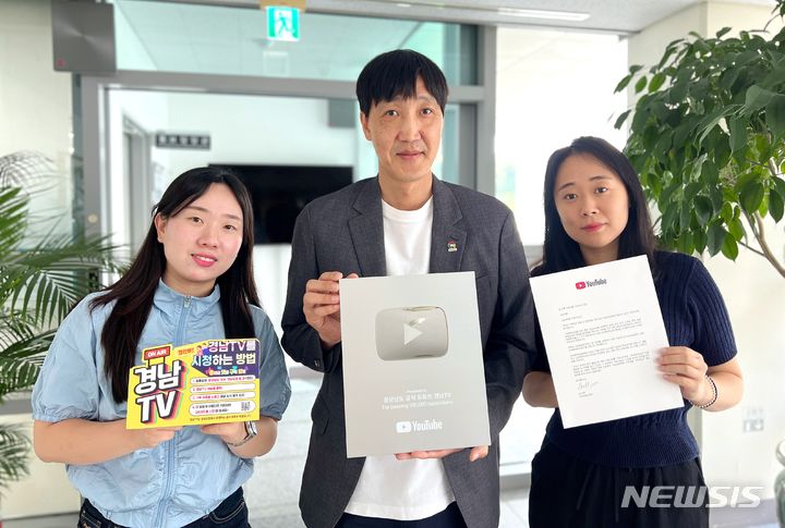 [창원=뉴시스]29일 경남도 장수환(가운데) 홍보담당관이 경상남도 공식 유튜브 채널 경남TV 구독자 수 10만 명 돌파에 따라 유튜브 본사로부터 받은 '실버버튼' 케이스를 들고 포즈를 취하고 있다.(사진=경남도 제공) 2024.07.29. photo@newsis.com 