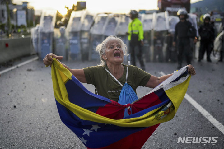[카라카스=AP/뉴시스] 29일(현지시각) 베네수엘라 카라카스에서 니콜라스 마두로 대통령의 3선 선거 결과에 반대하는 시위에 참여한 한 여성이 국기를 들고 도로를 봉쇄한 경찰과 대치하고 있다. 베네수엘라 대선을 둘러싼 부정·불공정 정황이 쏟아지면서 이에 항의하는 유권자들의 시위가 거세지고 있다. 2024.07.30.