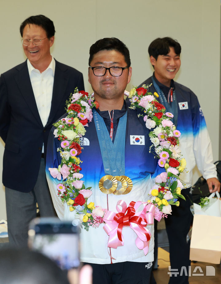 [인천공항=뉴시스] 고범준 기자 = 2024 파리 올림픽 양궁 전 종목에서 금메달을 획득한 대한민국 양궁 대표팀 김우진이 6일 오전 인천국제공항 제2여객터미널을 통해 귀국해 꽃목걸이를 걸고 어색해 하고 있다. 2024.08.06. bjko@newsis.com