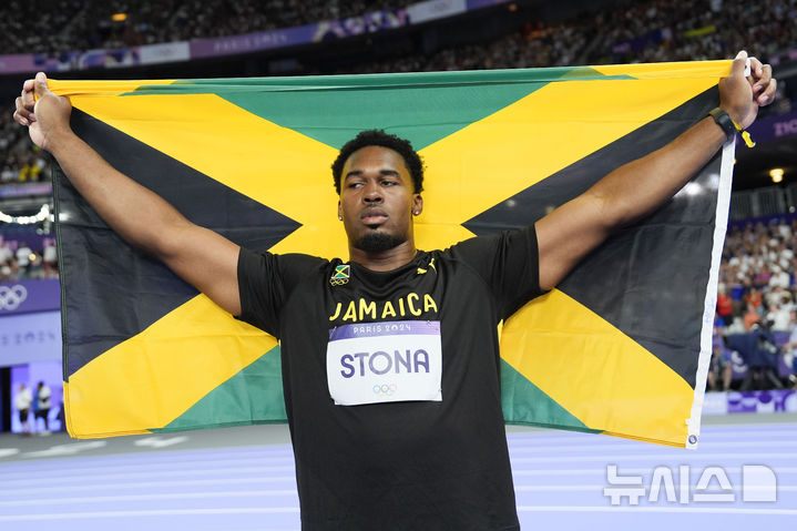 [파리=AP/뉴시스] 로제 스토나(자메이카)가 7일(현지시각) 프랑스 파리 스타드 드 프랑스에서 열린 2024 파리올림픽 육상 남자 원반던지기에서 우승한 후 국기를 두르고 세리머니하고 있다. 스토나는 70m00을 던져 올림픽 신기록(종전 69m89)을 세우며 자메이카 최초로 이 종목에서 금메달을 목에 걸었다. 2024.08.08.