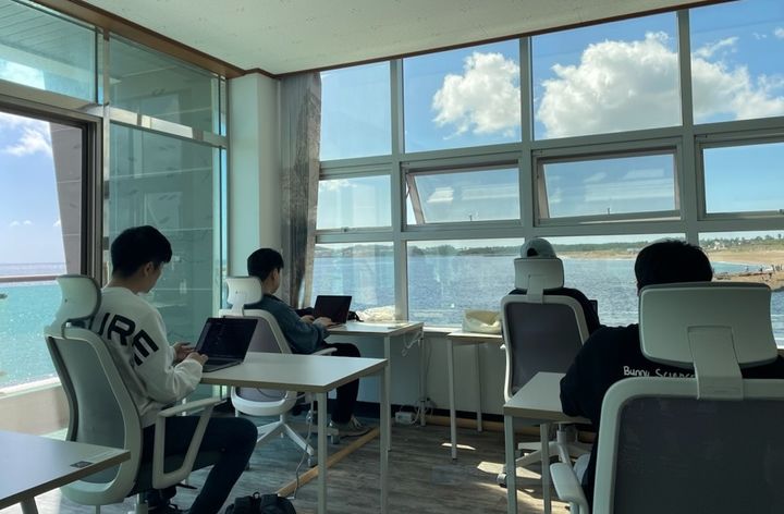 [서울=뉴시스] 제주 서귀포시 안덕면에 위치한 '사계마을'의 공유오피스에서 워케이션 참가자들이 창 밖의 바다 풍경을 배경으로 근무를 하고 있다. 2024.10.14. (사진=어촌어항공단 제공) *재판매 및 DB 금지