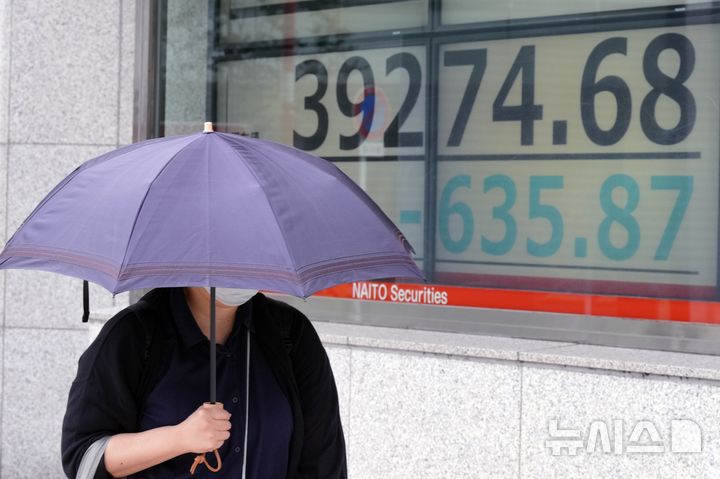 [도쿄=AP/뉴시스]16일 일본 도쿄에서 도쿄증시 주요 지수를 보여주는 증권사 전광판 앞을 한 시민이 지나가고 있다. 2024.10.16.