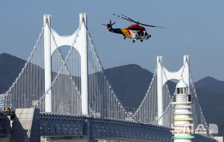 [부산=뉴시스] 하경민 기자 = 2024 재난대응 안전한국훈련-지진해일·화재 재난대응훈련이 열린 24일 부산 남구 용호별빛공원 앞 바다에서 남해해경청 헬기가 익수자를 구조한 뒤 광안대교를 지나고 있다.  이날 훈련에는 남구청과 부산해경, 해군작전사 등 14개 기관에서 300여 명이 참여했으며, 선박 8척과 헬기 1대 등이 동원됐다. 2024.10.24. yulnetphoto@newsis.com