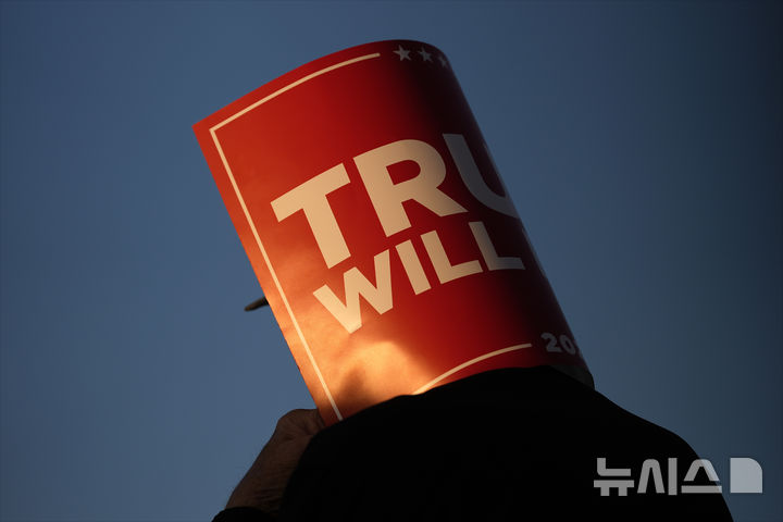 [킨스턴=AP/뉴시스] 3일(현지시각) 미국 노스캐롤라이나(NC)주 킨스턴 공항에서 공화당 대선 후보 도널드 트럼프 전 대통령의 지지자가 "트럼프가 해결할 것"(Trump Will Fix It)이라고 적힌 손팻말을 머리에 두르고 그의 연설을 듣고 있다. 2024.11.04.