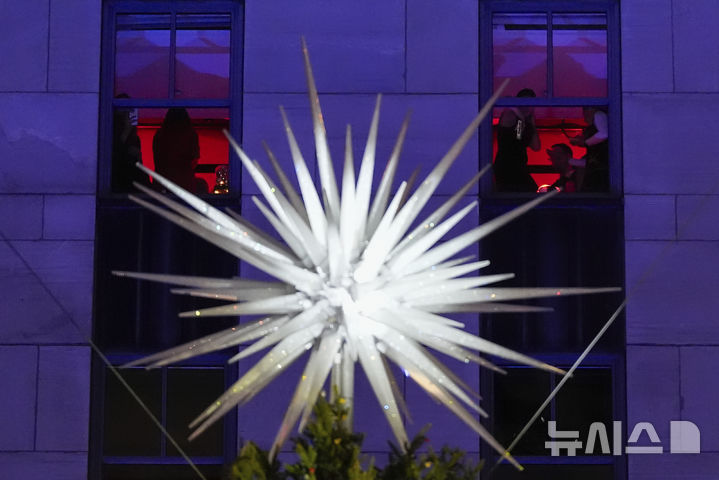 [뉴욕=AP/뉴시스] 4일(현지시각) 미국 뉴욕에 있는 록펠러 재단 앞에서 제92회 록펠러 센터 크리스마스트리 점등식이 열려 건물 내 사람들이 빛나는 스와로브스키 크리스털을 바라보고 있다. 2024.12.05.