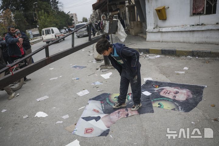 [하마=AP/뉴시스] 시리아 반군의 공세로 정권 붕괴를 맞은 바샤르 알아사드 시리아 대통령이 러시아 모스크바로 망명을 간 것으로 드러났다. 사진은 한 소년이 지난 7일(현지시각) 시리아 하마에서 바샤르 알아사드 시리아 대통령과 전임자인 그의 부친 하페즈 알아사드 전 시리아 대통령 사진을 밟고 서 있는 모습. 2024.12.08.