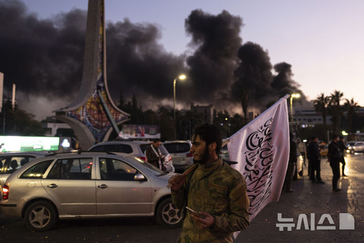 [다마스쿠스=AP/뉴시스] 8일(현지시각) 시리아 바샤르 알아사드 독재 정권 붕괴를 축하하기 위해 모여들고 있는 사람들 뒤로 검은 연기가 피어오르고 있다. 2024.12.09.