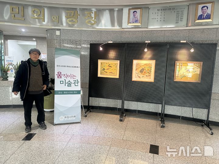 [화성=뉴시스] 김원기 작가가 화성시의회 로비에 설치된 자신의 작품 옆에서 사진을 찍고 있다.(사진=화성시의회 제공)2024.12.09.photo@newsis.com