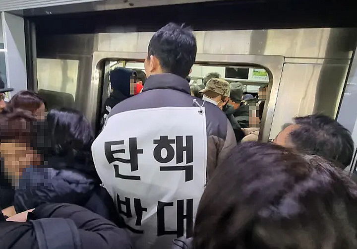 [서울=뉴시스] 윤석열 대통령 2차 탄핵소추안 국회 본회의 표결이 이뤄진 14일 서울 여의도 국회 앞과 광화문 광장에서 탄핵 찬반 집회가 열린 가운데 지하철에서 '탄핵 반대' 플래카드를 등에 걸고 시민들을 위협하는 남성에 대한 제보가 나왔다. (사진=유튜브 채널 '촛불행동tv') *재판매 및 DB 금지