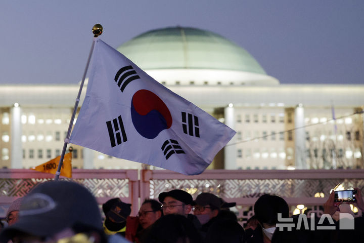 [서울=뉴시스] 최동준 기자 = 윤석열 대통령 탄핵안이 가결된 14일 서울 영등포구 국회 앞에서 열린 촛불집회 참가자가 태극기를 들고 있다. 2024.12.14. photocdj@newsis.com