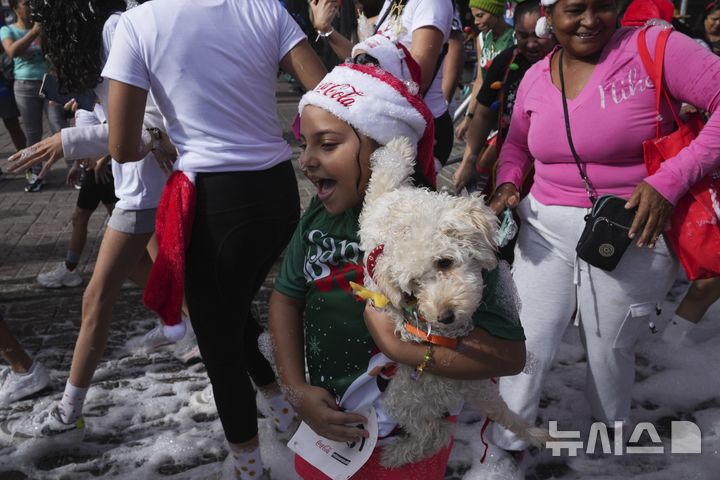 [카라카스=AP/뉴시스] 15일(현지시각) 베네수엘라 카라카스에서 '산타 런' 행사가 열려 한 어린이가 강아지를 안고 달리고 있다. 2024.12.16.