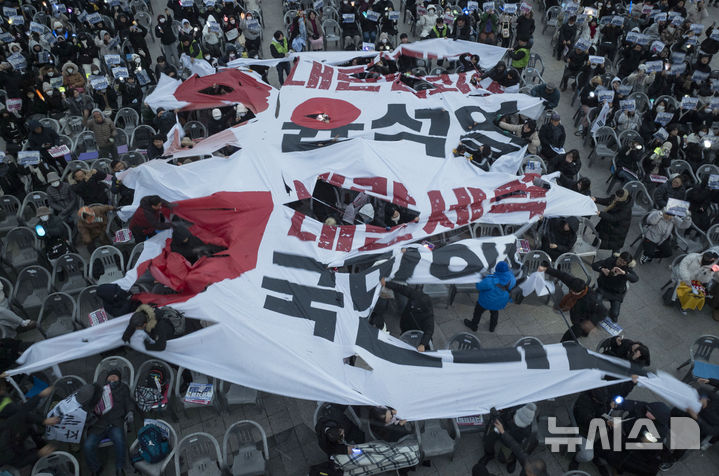 [광주=뉴시스] 이영주 기자 = 광주시민들이 21일 오후 광주 동구 5·18민주광장에서 열린 윤석열정권 즉각퇴진·사회대개혁 광주비상행동의 7차 광주시민총궐기대회에 참여해 윤석열 대통령과 국민의힘을 비판하는 대형 현수막을 찢고 있다. 2024.12.21. leeyj2578@newsis.com