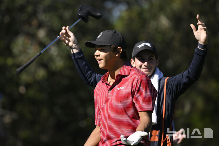 Charlie Woods, front, and his caddie Luke Wise react after his hole-in-one on the fourth hole during the final round of the PNC Championship golf tournament, Sunday, Dec. 22, 2024, in Orlando, Fla. (AP Photo/Phelan M. Ebenhack)