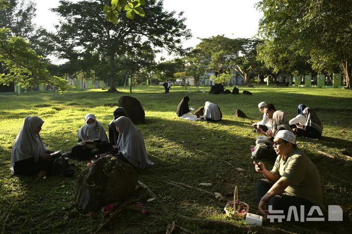 [AP/뉴시스] 인도네시아 북서단 아체주 주도 반다 아체에 있는 2004년 쓰나미 희생자 집단매장지 풀밭. 26일 20주년을 맞아 사람들이 모여 추모하고 있다. 