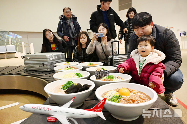 [도쿠시마(일본)=뉴시스] 전신 기자 = 26일 일본 도쿠시마공항에서 열린 '이스타항공 도쿠시마 첫 취항' 기념 행사에서 탑승객들이 공항 수하물 컨베이어 벨트에 전시된 '도쿠시마 특산물 대형 라멘 모형'을 관람하고 있다.이스타항공이 국내 최초로 단독 취항하는 인천-도쿠시마 노선은 주 3회(화, 목, 토) 운항한다. (공동취재) 2024.12.26. photo1006@newsis.com