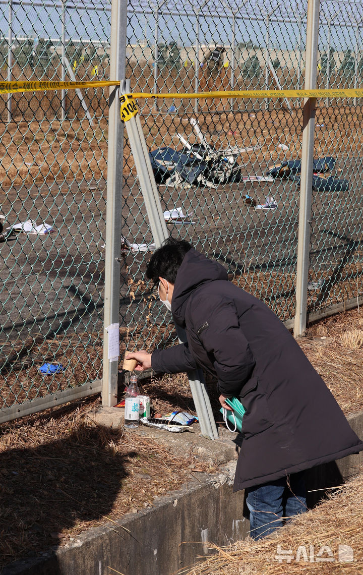 [무안=뉴시스] 이영환 기자 = 31일 오전 전남 무안국제공항 제주항공 여객기 충돌 사고 현장을 찾은 조문객이 술을 뿌리고 있다. 2024.12.31. 20hwan@newsis.com