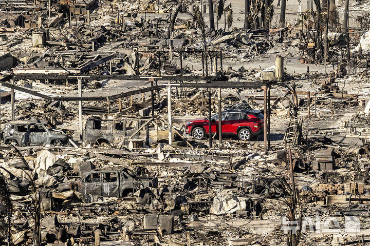 [로스앤젤레스=AP/뉴시스] 12일(현지 시간) 미 캘리포니아주 로스앤젤레스 인근 퍼시픽 팰리세이즈에서 자동차 한 대가 '팰리세이즈 파이어' 산불로 파괴된 집과 차량 잔해 사이를 지나가고 있다. 2025.01.14.