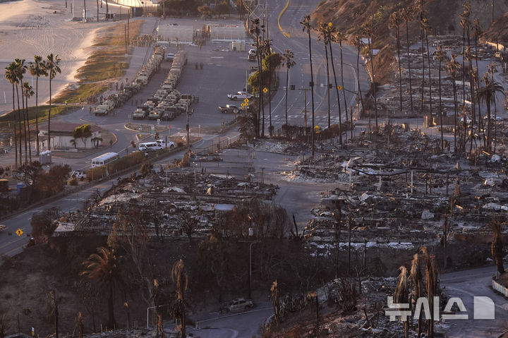 [로스앤젤레스=AP/뉴시스] 12일(현지 시간) 캘리포니아 로스앤젤레스의 퍼시픽 팰리세이즈에서 주 방위군 차량 여러 대가 해변을 따라 줄 서 있는 모습. 고속도로를 따라 불에 탄 동네가 보인다. LA 산불 사망자는 이날 기준 24명으로 증가했다. 2025.01.13.