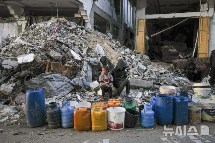 [가자시티=AP/뉴시스] 5일(현지 시간) 이스라엘군의 공습과 지상 공격으로 크게 파괴된 가자지구 가자시티에서 두 어린이가 줄지어 놓인 빈 물통 옆에 앉아 물 받기 순서를 기다리고 있다. 2025.02.06.
