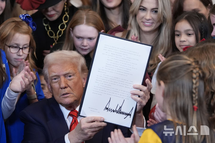 [워싱턴=AP/뉴시스] 도널드 트럼프 미국 대통령이 2월 5일 백악관 이스트룸에서 여자 선수들이 지켜보는 가운데 성전환 여성 운동선수의 여성·소녀 운동 경기 참가를 금지하는 행정명령에 서명하고 이를 들어 보이고 있다.  7월 21일에는 미국 올림픽 패럴림픽 위원회도 트럼프의 이 명령을 따라줄 것을 산하 체육단체들에게 명령했다. 2025.07.23.