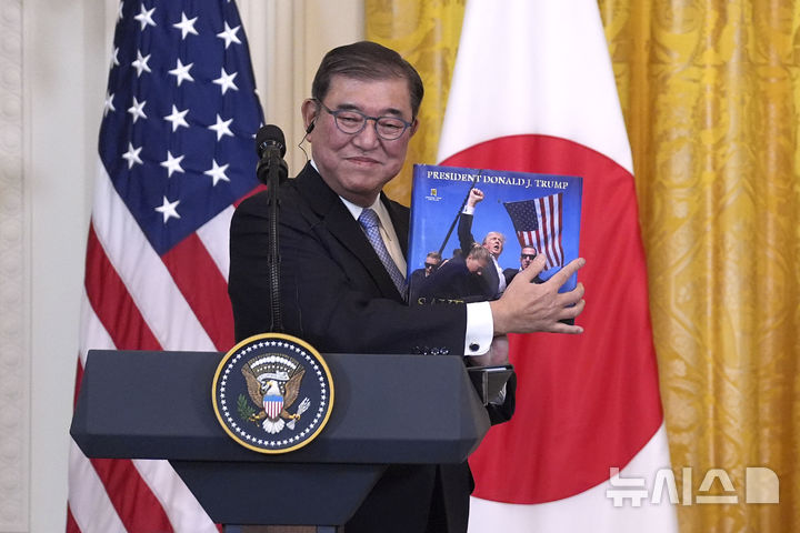 [워싱턴=AP/뉴시스] 이시바 시게루 일본 총리가 7일(현지 시간) 백악관에서 도널드 트럼프 미국 대통령과 회담 후 공동 기자회견을 하면서 트럼프 대통령으로부터 선물 받은 사진집을 들어 보이고 있다. 2025.02.08.