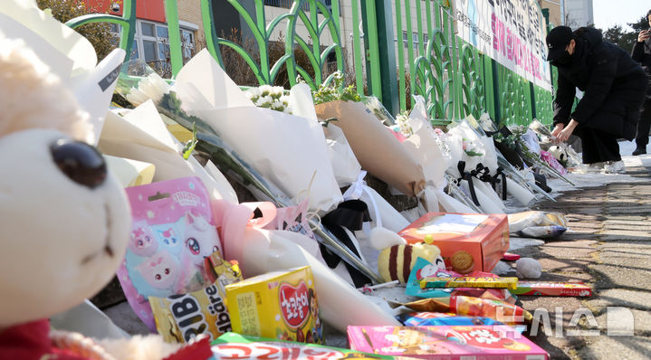 [대전=뉴시스] 강종민 기자 = 11일 오후 초등학생 피살사건이 발생한 대전 서구 관저동의 한 초등학교 정문 옆 담장에서 시민들이 국화꽃과 과자·음료 등을 놓으며 고 김하늘(7) 양을 추모하고 있다. 2025.02.11. ppkjm@newsis.com
