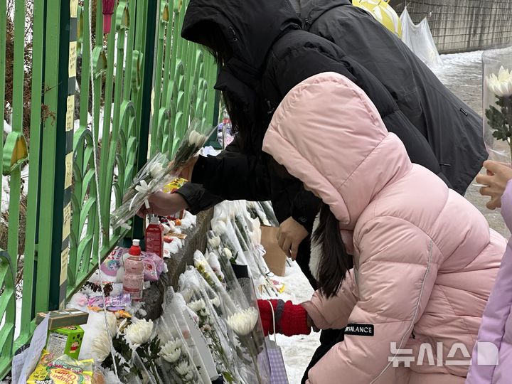 [대전=뉴시스] 김도현 기자 = 12일 오후 초등학생 피살 사건이 발생한 대전 서구 관저동의 한 초등학교 정문 옆 담장에서 김하늘(7)양을 추모하는 아이와 부모가 꽃을 내려놓고 있다. 2025.02.12. kdh1917@newsis.com