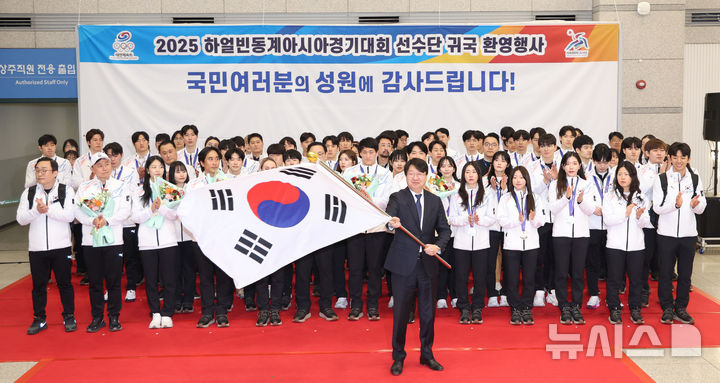 [인천공항=뉴시스] 김진아 기자 = 15일 인천국제공항 제1터미널에서 열린 2025 하얼빈 동계 아시안게임 한국 선수단 귀국 환영행사에서 윤성욱 대한체육회 사무총장이 단기를 받아 흔들고 있다. 2025.02.15. bluesoda@newsis.com