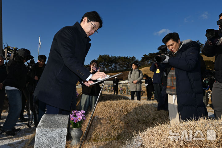 [광주=뉴시스] 이영주 기자 = 김경수 전 경남도지사가 24일 오전 광주 북구 운정동 국립5·18민주묘지를 찾아 한강 작가의 소설 '소년이 온다' 속 주인공 고(故) 문재학 열사의 생애를 알리는 알림판 위에 쌓인 눈을 닦고 있다. 2025.02.24. leeyj2578@newsis.com