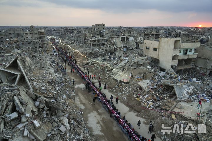 [라파=AP/뉴시스] 이스라엘은 지난 2일(현지 시간) 팔레스타인 무장정파 하마스에 '휴전 1단계' 연장 수용을 압박하기 위해 가자지구에 대한 구호품 반입을 중단했다. 사진은 라마단 첫날인 1일 가자지구 남부 라파에서 팔레스타인 주민들이 파괴된 집과 건물 잔해에 둘러싸인 커다란 식탁에 모여 앉아 이프타르(금식 종료 후 식사)를 함께하는 모습. 2025.03.02.