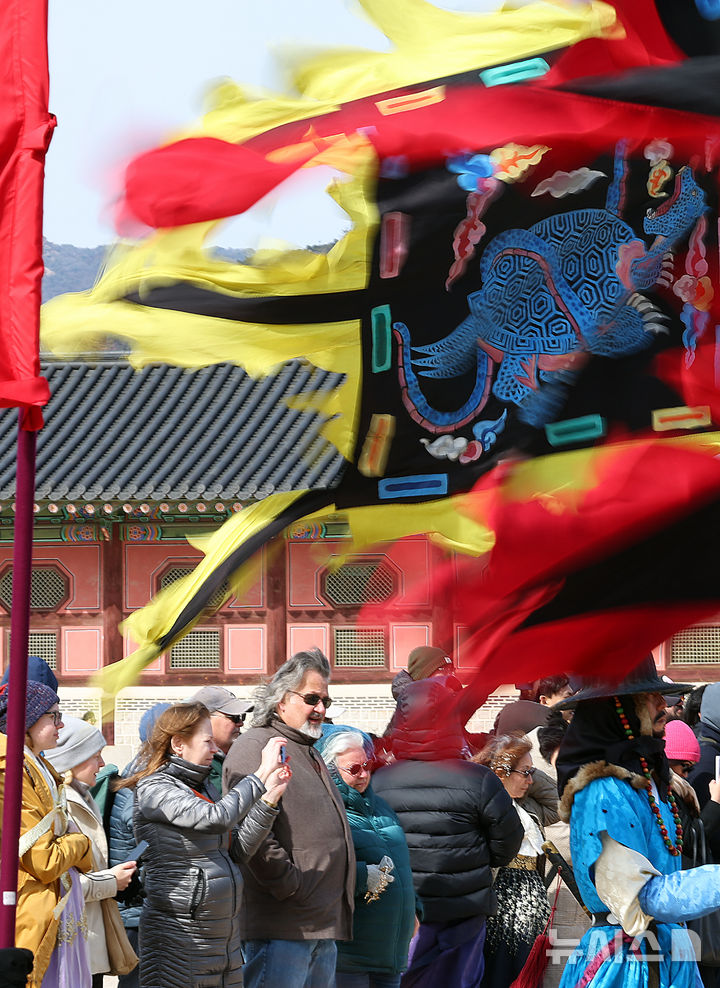 [서울=뉴시스] 최진석 기자 = 북동풍의 영향으로 기온이 떨어진 3일 서울 종로구 경복궁에서 수문장 교대식을 지켜보는 외국인 앞으로 깃발이 바람에 펄럭이고 있다. 2025.03.03. myjs@newsis.com