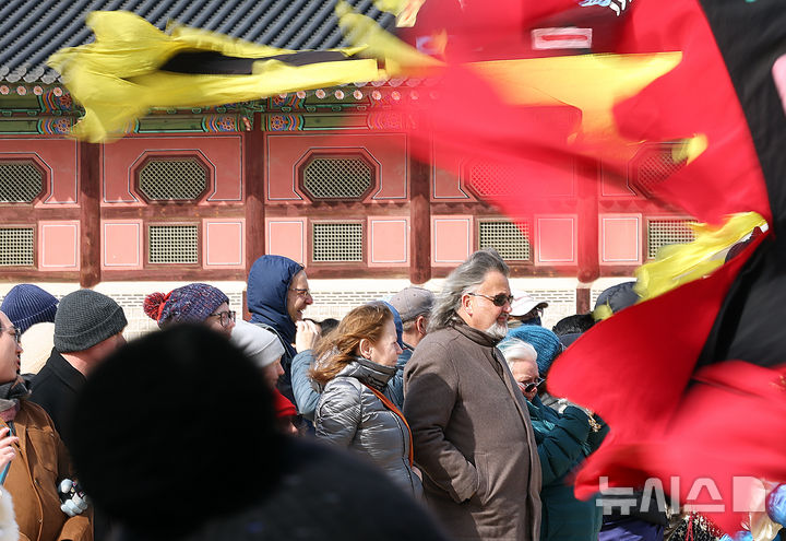 [서울=뉴시스] 최진석 기자 = 북동풍의 영향으로 기온이 떨어진 3일 서울 종로구 경복궁에서 수문장 교대식을 지켜보는 외국인 앞으로 깃발이 바람에 펄럭이고 있다. 2025.03.03. myjs@newsis.com